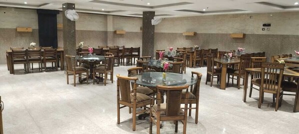 A spacious dining area with multiple round tables and wooden chairs, arranged in a grid pattern. - Surya Continental (Lucknow)