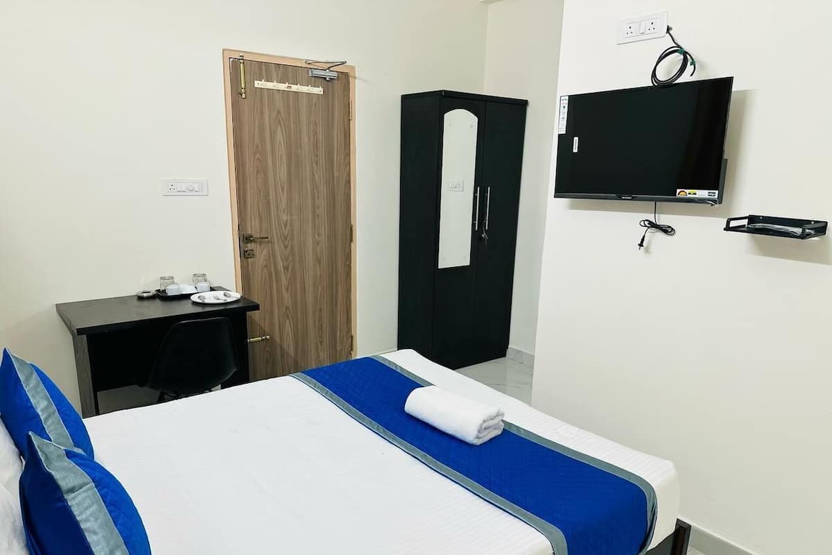 Quarto de hotel com cama, escrivaninha, guarda-roupa e televisão.