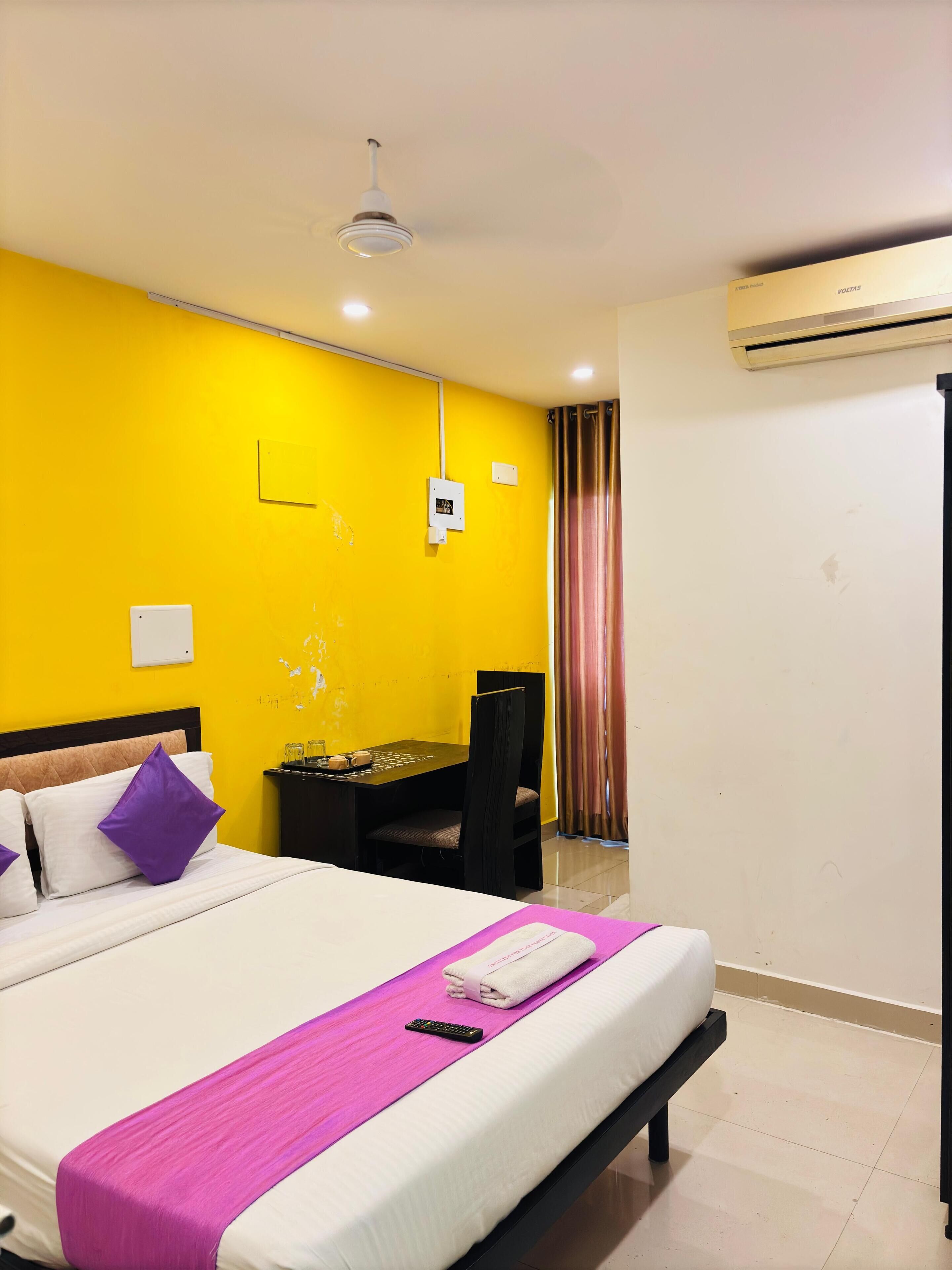 A hotel room with a bed, a desk, and an air conditioning unit.