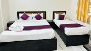 A hotel room with two beds, each with a black headboard, white bedding, and purple pillows. There is a yellow curtain on the window and a white wall. - S V COMFORTS (Bengaluru)