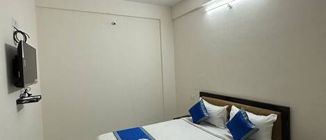 Una habitación de hotel con una cama, una mesita de noche con una bandeja de desayuno, un ventilador de techo y un televisor montado en la pared.