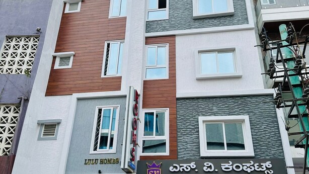 A multi-story building with a modern architectural design, featuring a mix of grey, brown, and white facades. The ground floor has a storefront with signage for 'SV COMFORTS' and 'Lulu Homes'. - S V COMFORTS (Bengaluru)