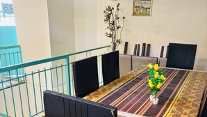A dining area with a long table, chairs, and a vase of yellow flowers. - S V COMFORTS (Bengaluru)
