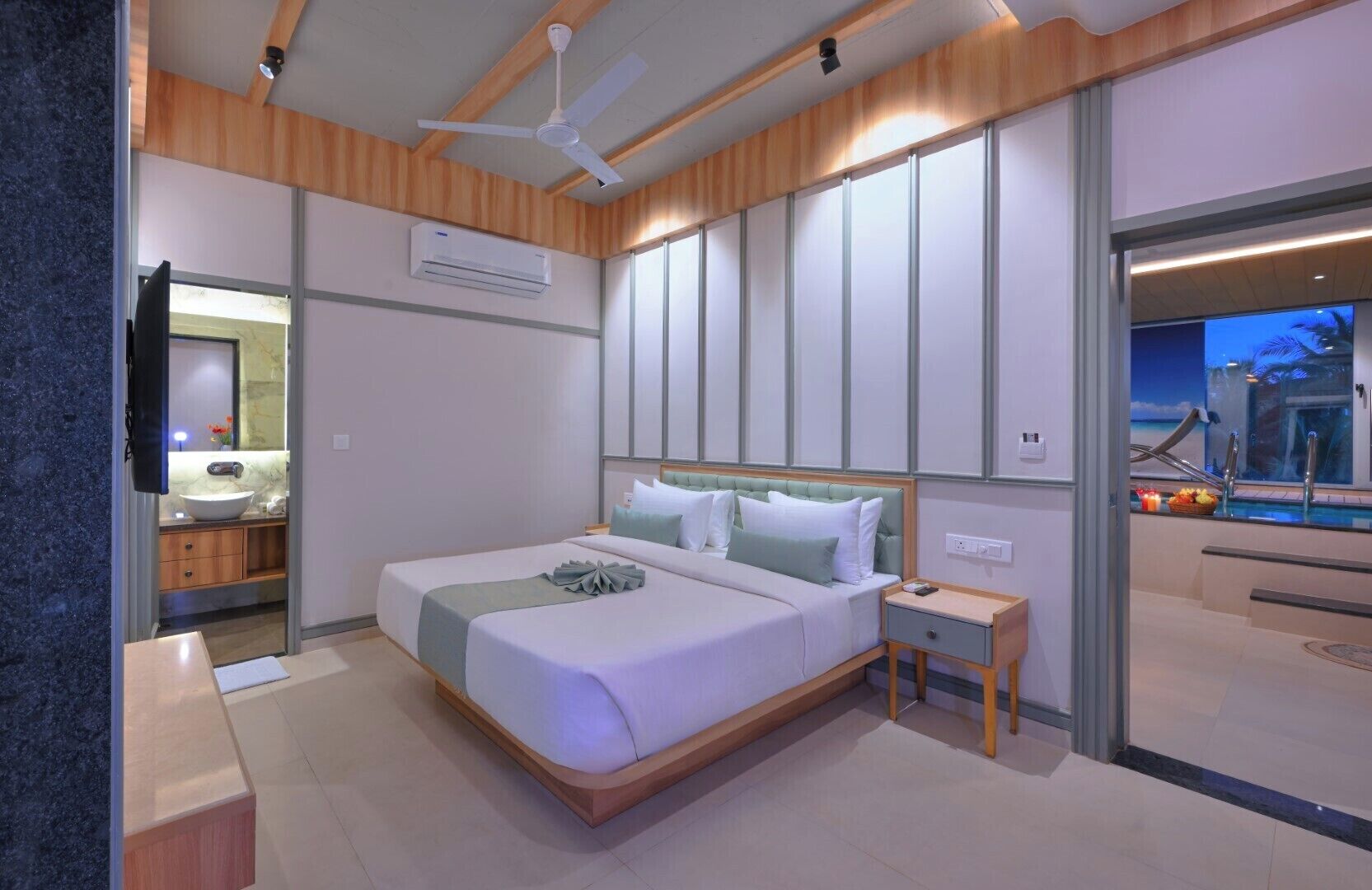 Una camera d'albergo moderna con un letto grande, un comodino, una TV integrata e una finestra con vista sulla spiaggia.