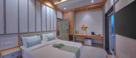 A modern hotel room with a large bed, a bedside table, a vanity with a mirror, and a small desk with a chair.
