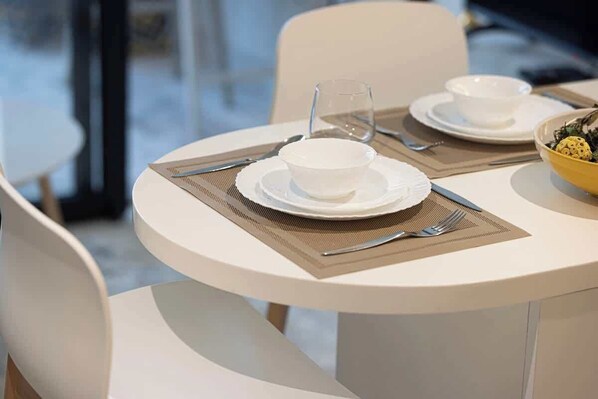 A dining table set with white plates, bowls, cutlery, and a glass.