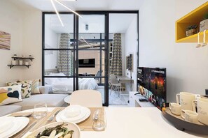 A modern hotel room with a dining area, a TV, and a bookshelf.