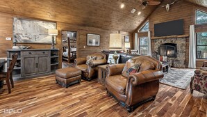 Ein rustikales Interieur mit Holzdielenböden, Ledermöbeln, einem Kamin aus Stein und großen Fenstern.