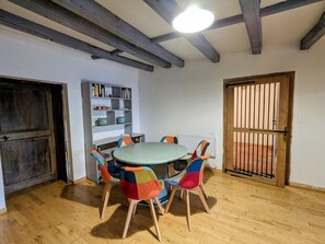 A room with a round table, colorful chairs, a bookshelf, a radiator, and a wooden door with a metal gate. - Renovated cottage in Mauvages with garden, BBQ and WIFI (Mauvages)
