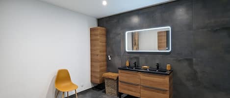 A modern bathroom with a wooden vanity, a large mirror, and a yellow chair.