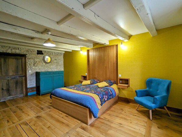 A bedroom with a wooden bed, a blue chair, and a stone wall. - Renovated cottage in Mauvages with garden, BBQ and WIFI (Mauvages)