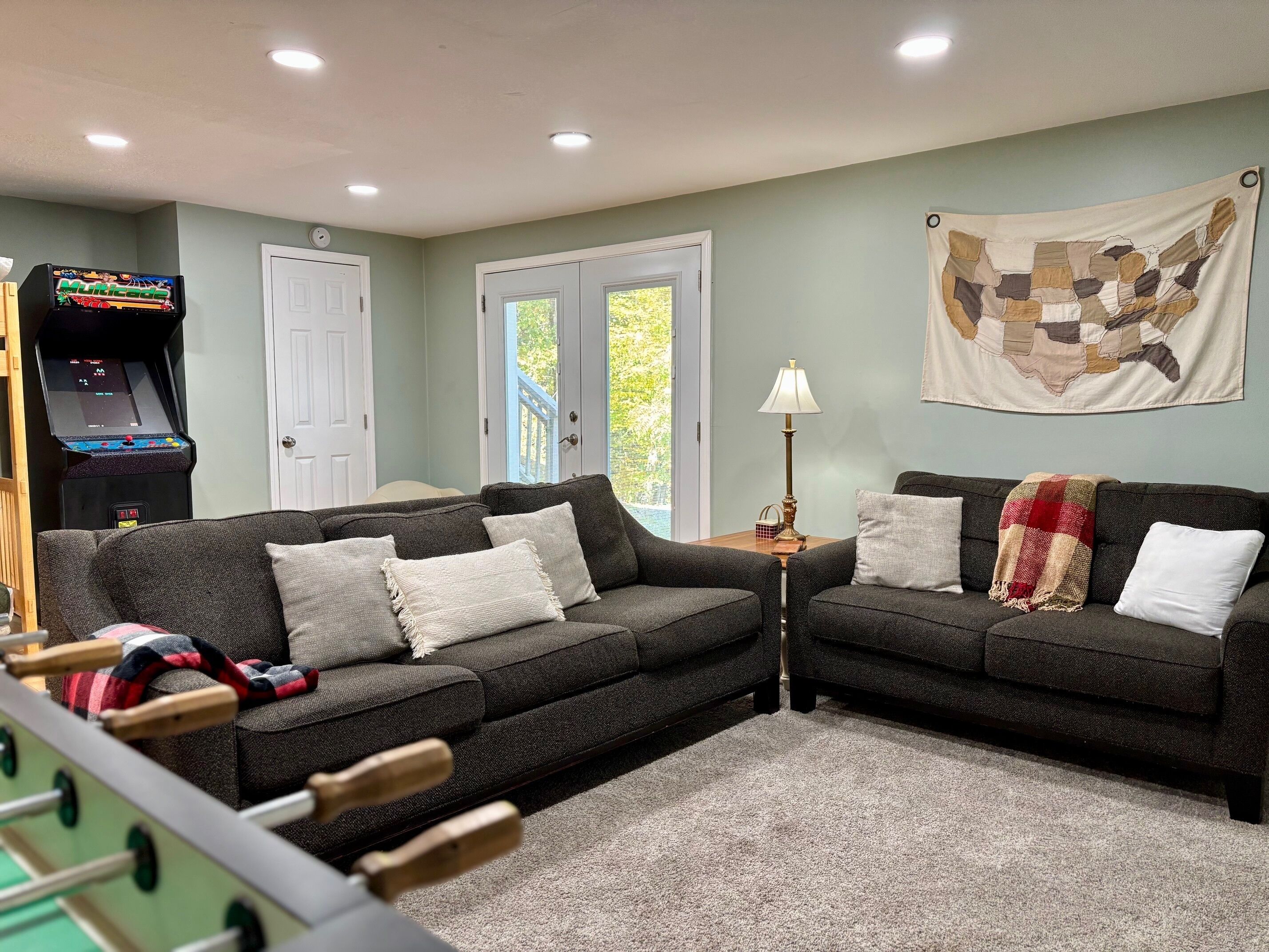 A living room with two dark sofas, a foosball table, a lamp, and a wall map.