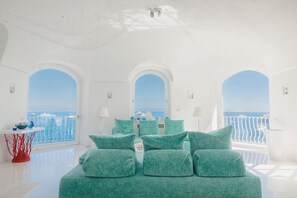 A bright, white room with a large bed, multiple windows, and a view of the sea. - Villa Beatrice by Elite Villas (Capri)