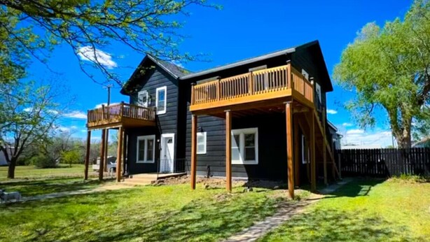 Une maison à deux étages avec une terrasse en bois et une cour arrière clôturée.