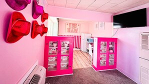 Une pièce décorée dans des tons roses, comprenant un coin cuisine, un téléviseur et un panneau indiquant « FOIN GRATUIT ».