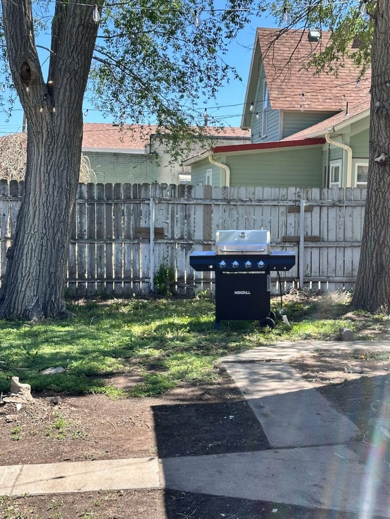 Ein Garten mit Grill, Holzzaun und Haus im Hintergrund.
