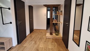 A hallway with wooden flooring, dark doors, and a central wooden shelf with decorative items. - Charming cottage between forest and relaxation with spa and WIFI (Ville-sur-Illon)