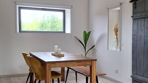 A dining area with a wooden table, four chairs, a window, a plant, and a mirror on the wall. - Charming cottage between forest and relaxation with spa and WIFI (Ville-sur-Illon)