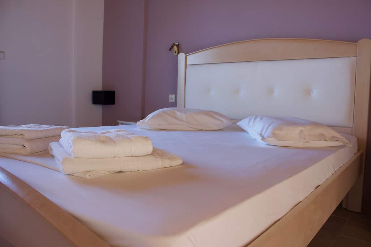 A neatly made bed with white linens and towels, a wooden headboard, and a wall-mounted light fixture.