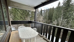 Ein überdachter Balkon mit einem weißen Tisch und Stühlen, mit Blick auf ein bewaldetes Gebiet.