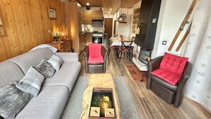 Ein gemütliches Wohnzimmer mit einer Couch, Sesseln und einem Couchtisch. Im Hintergrund ist eine Essecke mit Tisch und Stühlen zu sehen.