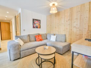 A modern living room with a grey sectional sofa, a round wooden coffee table, and a wooden accent wall. - Modern duplex for 8, central Morzine, near lifts (Morzine)
