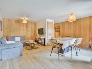 A modern living room with a sofa, coffee table, TV, and dining area with chairs and a table.