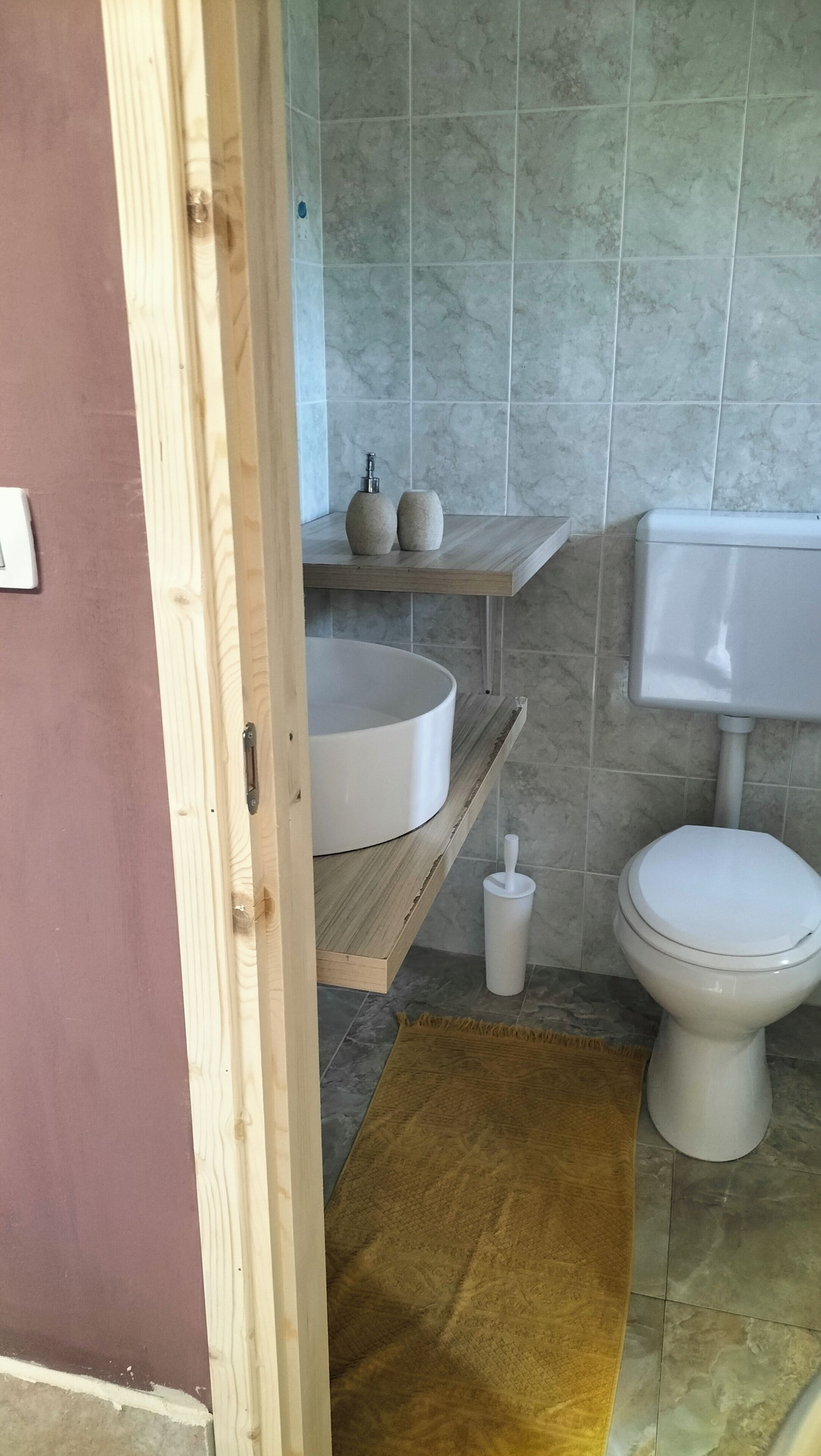 A bathroom with a wooden vanity, a white sink, a toilet, and a marble-tiled wall.