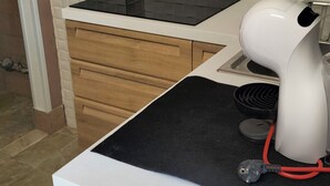 A kitchen with a white countertop, a black induction cooktop, a white appliance with a red cord, and wooden cabinets. - Detached house with two entrances and parking space on private road, convenient and new (Gallipoli)