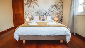 A bedroom with a bed, wooden floor, a door, and a wall with a tropical mural. - Villa LONTAN (Entre-Deux)