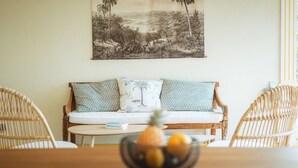 A cozy living area with a wooden sofa, two patterned pillows, and a bowl of fruit on a table. - Villa LONTAN (Entre-Deux)