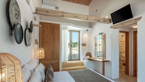 A bedroom with a bed, a wooden wardrobe, a window with a view, a mirror, and a television mounted on the wall. - Villa Froudi (Azogiras)