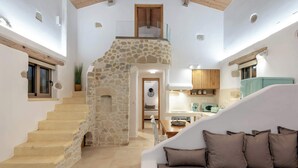 A spacious living area with a stone staircase, a white sofa, and a kitchen area with wooden cabinets and a teal refrigerator. - Villa Froudi (Azogiras)