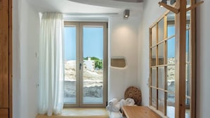 A bathroom with a wooden bench, a towel rack, and a view of the beach through a glass door. - Villa Froudi (Azogiras)