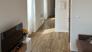 A spacious living area with a wooden floor, a flat-screen TV on a white stand, a brown sofa, and a wooden ceiling. - Casa Bice - A new apartment in the center of Tesino (Castello Tesino)