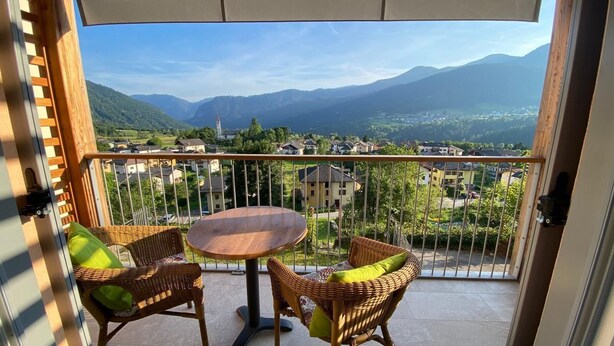 A balcony with wicker chairs and a table, offering a view of a town and mountains. - Casa Bice - A new apartment in the center of Tesino (Castello Tesino)