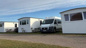Un parque para caravanas con varias caravanas y una furgoneta blanca estacionada al frente.