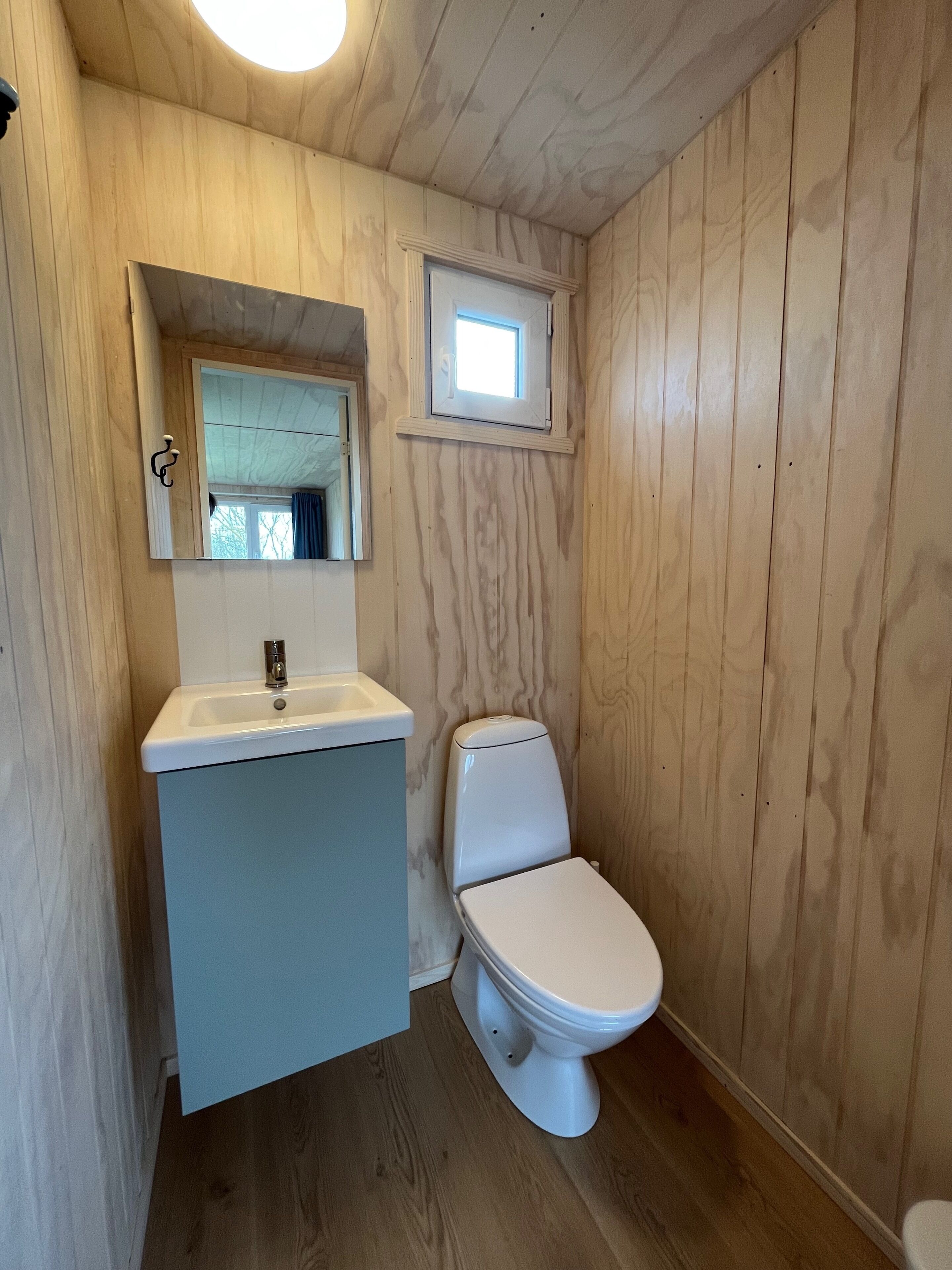 A small, wooden-paneled bathroom with a white sink, a toilet, and a mirror above the sink.