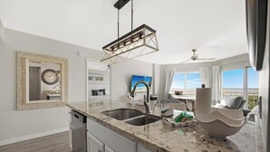 Une cuisine moderne dotée de plans de travail en granit, d’un évier à deux bacs et d’un luminaire suspendu.