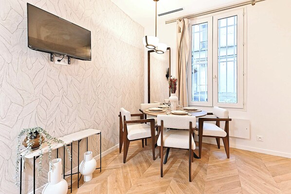 Un coin repas avec une table ronde dressée pour quatre personnes, entourée de chaises en bois. Un téléviseur à écran plat est fixé au mur, au-dessus de la table.