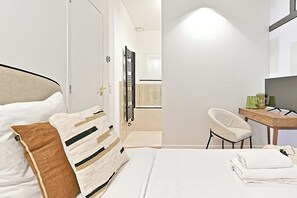 Een moderne hotelkamer met een bed, een stoel, een bureau met een computer en een televisie.