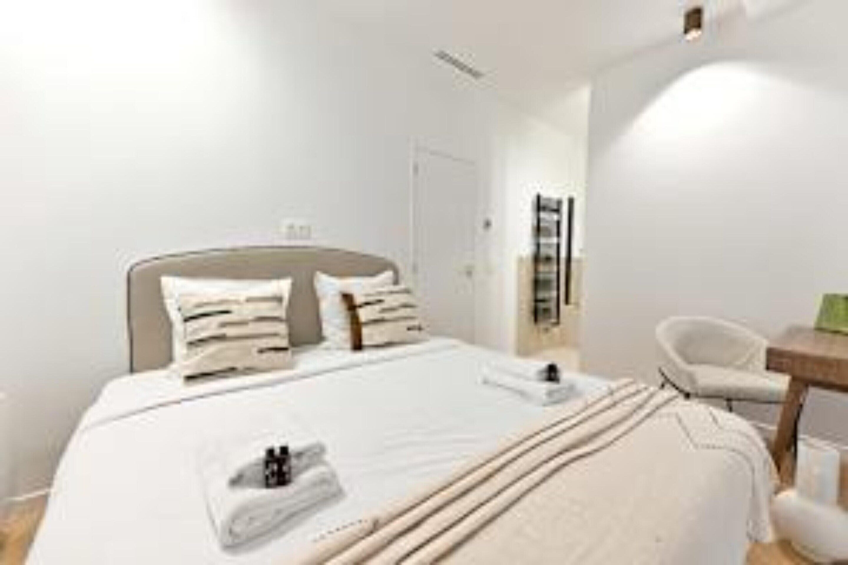 A modern hotel room with a large bed, a bedside table, a chair, and a small desk.