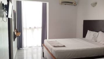 A hotel room with a bed, a bedside table, a wall-mounted air conditioner, and a window with curtains.
