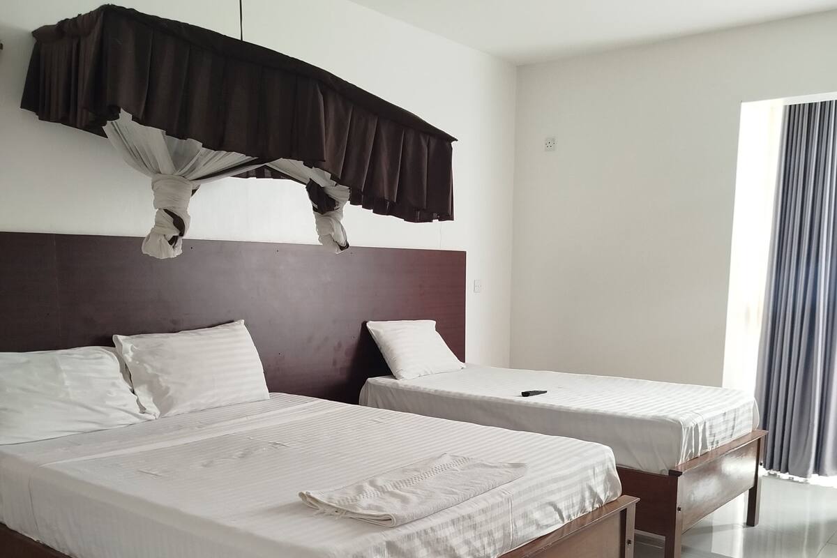 Habitación de hotel con dos camas, ventilador de techo y una ventana grande con cortinas.