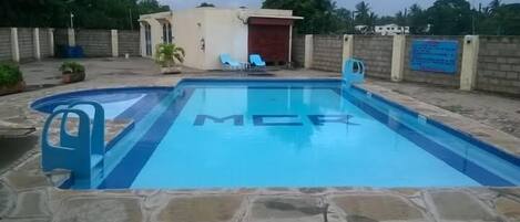 A swimming pool with the letters "MCR" on the water, surrounded by stone tiles.