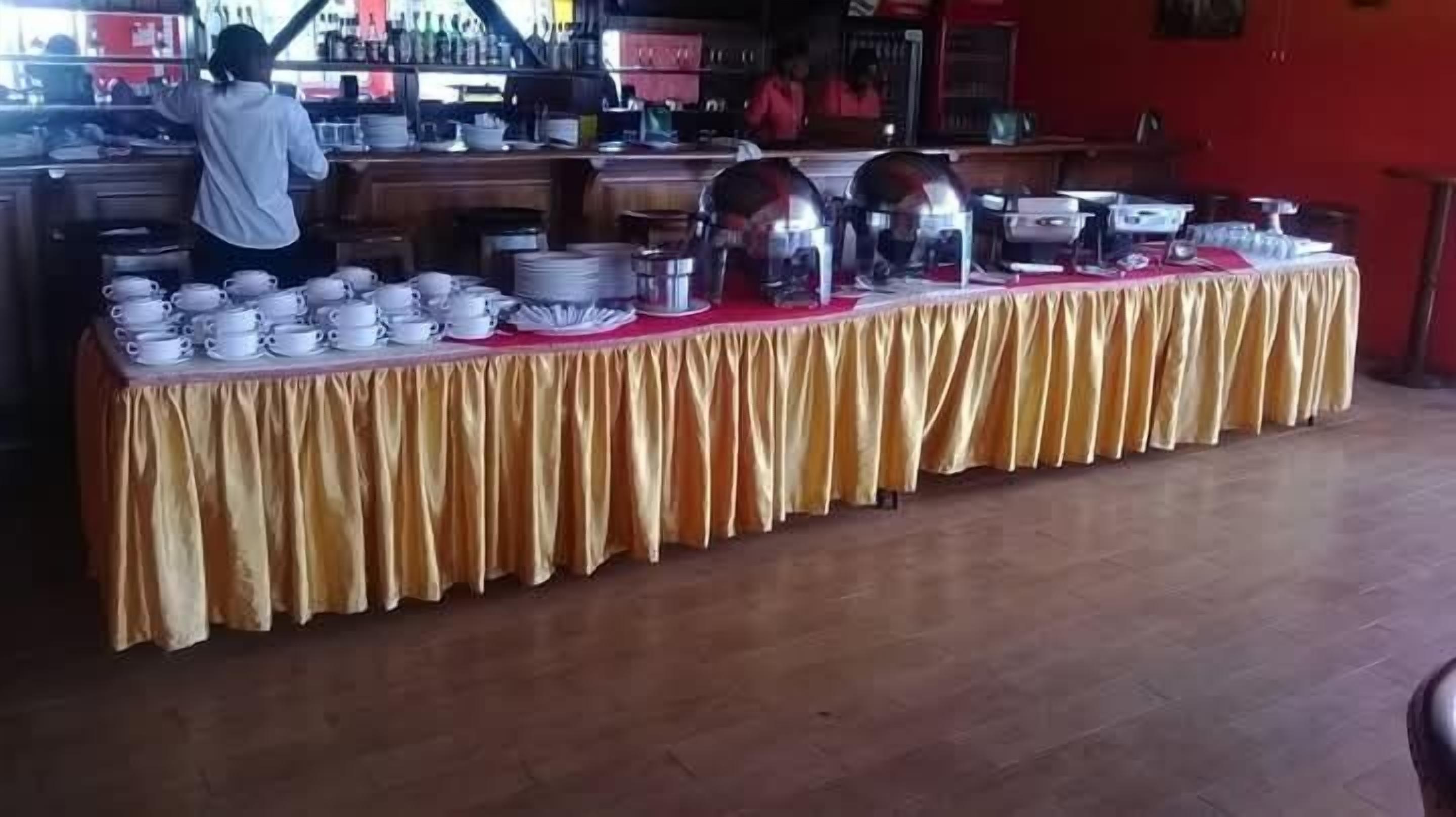A buffet setup with a variety of dishes and utensils on a table covered with a yellow cloth.