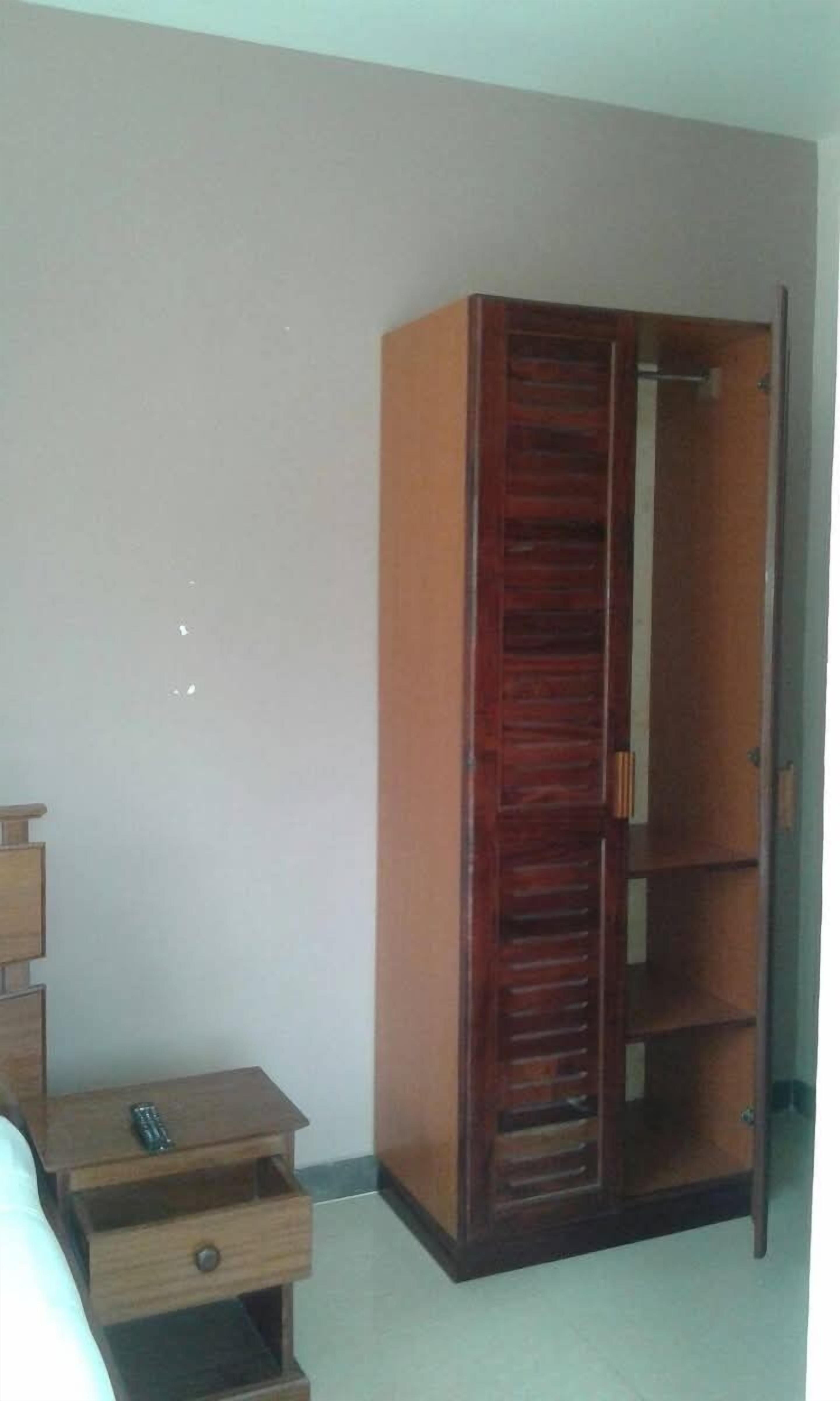 Una camera da letto con un'armadio in legno, un comodino di legno con un telecomando e un letto.