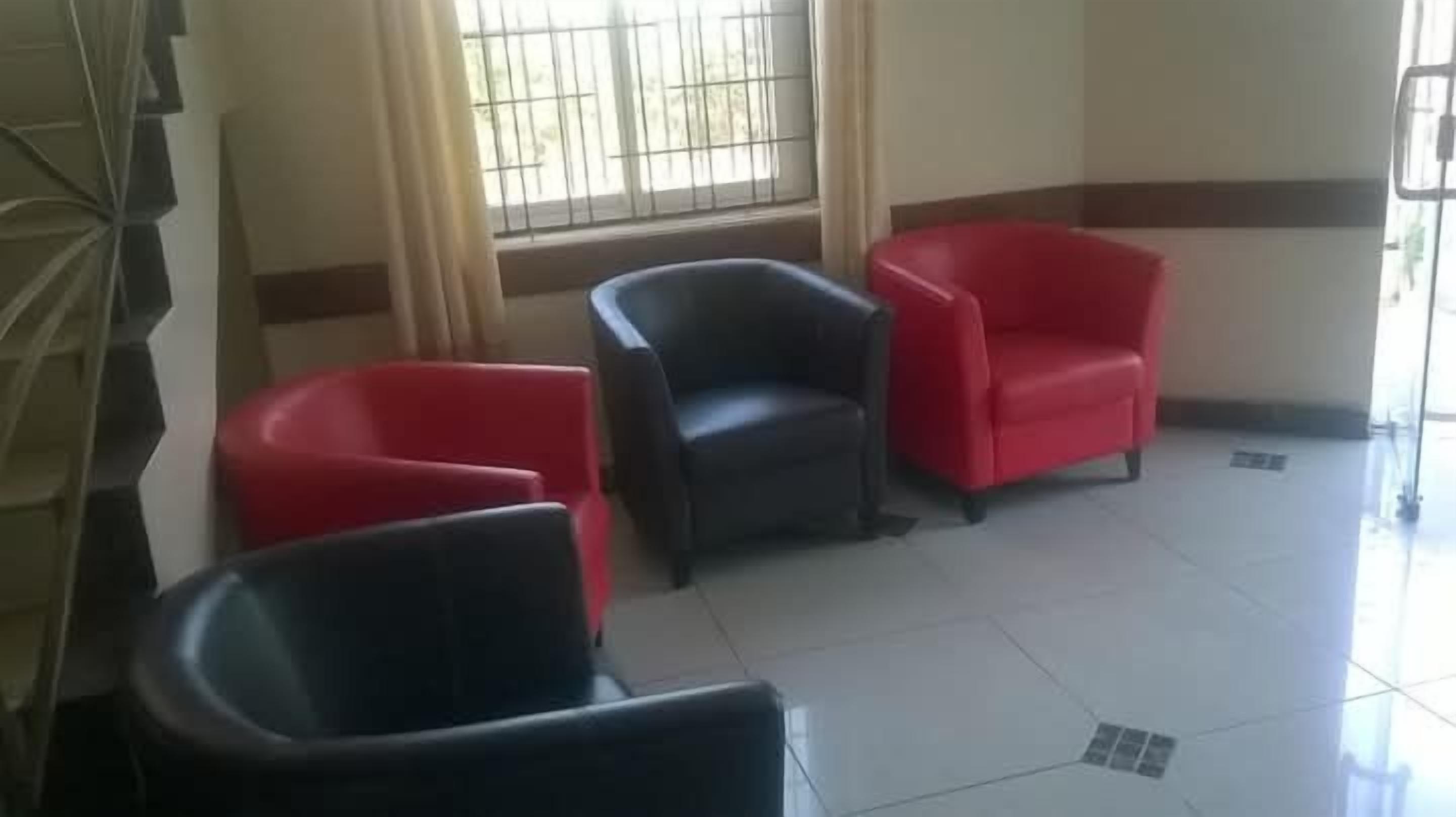 Une salle d’attente avec trois chaises, une fenêtre grillagée et un sol carrelé.