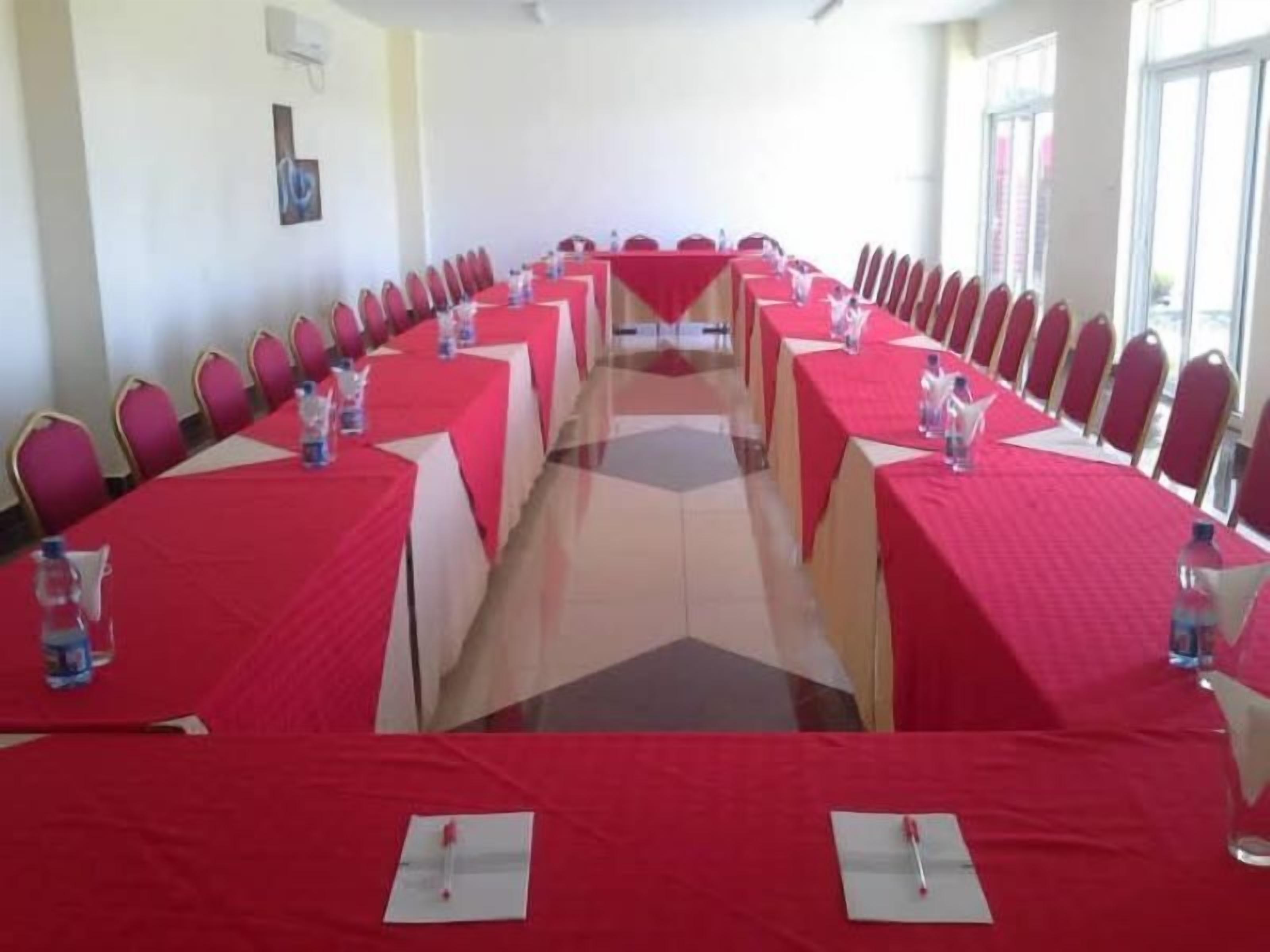 Une salle de conférence avec de longues tables, des nappes rouges et des chaises rouges.