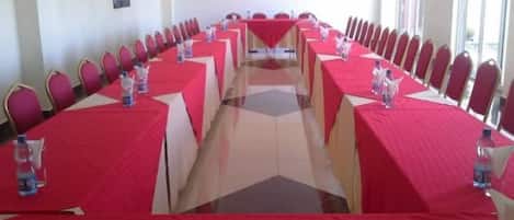 Une salle de conférence avec de longues tables, des nappes rouges et des chaises rouges.